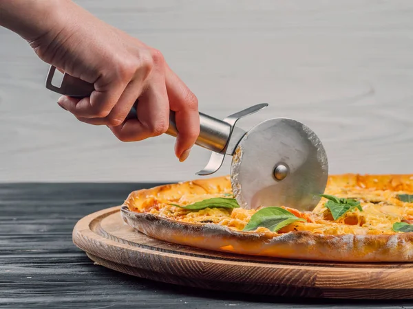 鋼のアクアパッツァ カッター。切断分離された木製のスタンドにおいしいイタリア料理。ナイフで女性の手がクローズ アップ ホワイト バック グラウンドでピザをカット — ストック写真