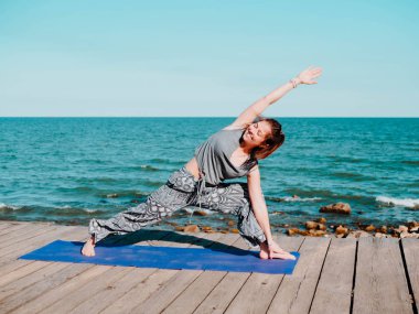 Genç güzel sportif kadın rahat giyim yoga asana suya yakın deniz plajında yapıyor. Kız pratik egzersizleri. Sağlık kavramı. Renkli resim.