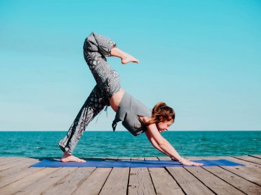 Genç güzel sportif kadın rahat giyim yoga asana suya yakın deniz plajında yapıyor. Kız pratik egzersizleri. Sağlık kavramı. Renkli resim.