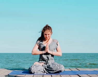 Genç güzel sportif kadın Yoga mudra suya yakın deniz ahşap plajda yapıyor. Kız pratik egzersizleri. Namaste elinde. Şükran işareti. Sağlık kavramı.