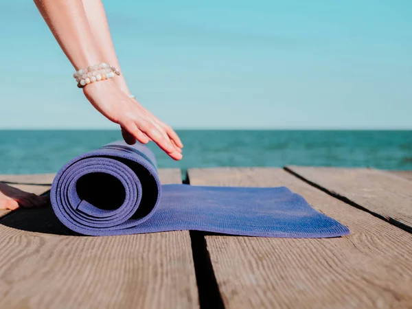 Giovane bella donna sportiva che si prepara per lo yoga asana sulla spiaggia di mare vicino all'acqua. Ragazza che copre stuoia viola. Concetto sanitario . — Foto Stock