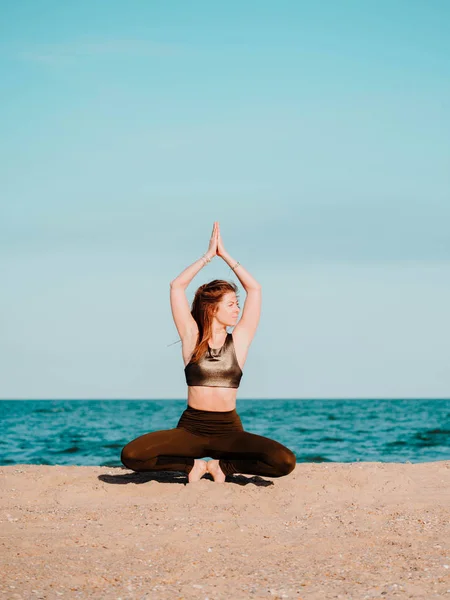 Giovane bella donna sportiva in costume verde facendo yoga asana sulla spiaggia vicino all'acqua. Ragazza che pratica esercizi. Concetto di salute. Copia spazio . — Foto Stock