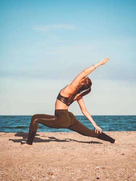 Молода красива спортивна жінка в зеленому одязі робить йогу асану на морському піщаному пляжі біля води. Дівчина практикує вправи. Концепція здоров'я. Копіювати простір . — стокове фото