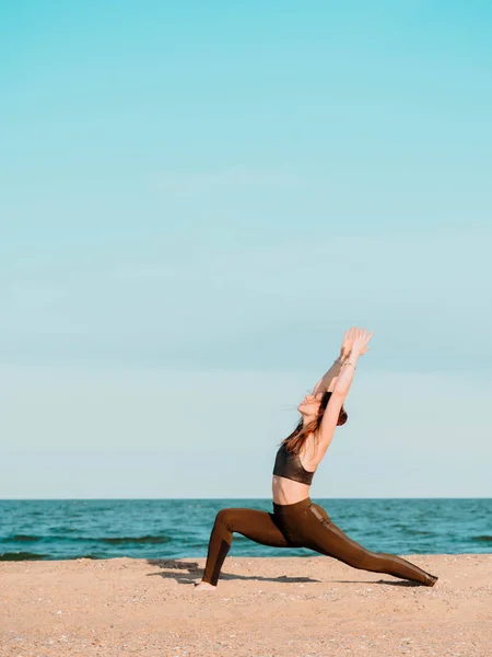 Giovane bella donna sportiva in abbigliamento verde facendo yoga asana sulla spiaggia di sabbia marina vicino all'acqua. Ragazza che pratica esercizi. Concetto di salute. Copia spazio . — Foto Stock