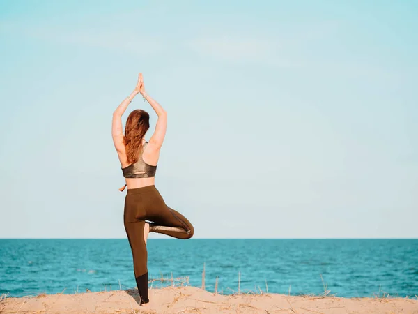 Fiatal, gyönyörű sportos nő zöld ruhát csinál jóga asana a tenger homokos strand közelében a víz. Lány gyakorló gyakorlatok. Egészségügyi koncepció. Másolja a hely. — Stock Fotó