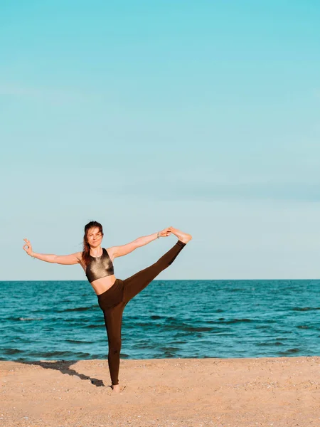 Fiatal, gyönyörű sportos nő zöld ruhát csinál jóga asana a tenger homokos strand közelében a víz. Lány gyakorló gyakorlatok. Egészségügyi koncepció. Másolja a hely. — Stock Fotó