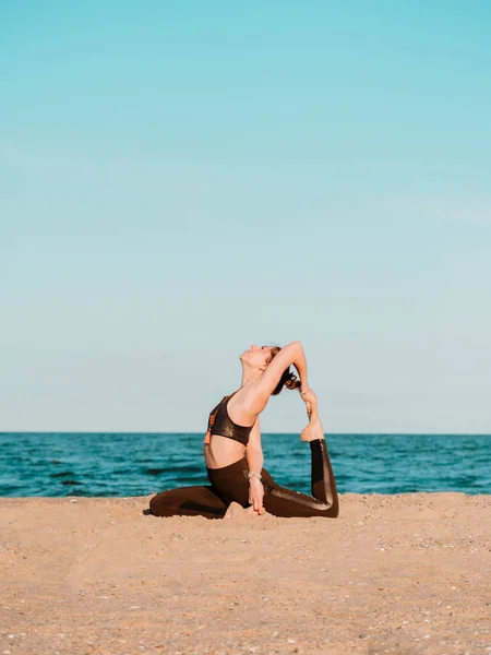 Fiatal, gyönyörű sportos nő csinál jóga asana a tengeri strand közelében a víz zöld ruha és a mala gyöngyök. Lány gyakorló gyakorlatok. Egészségügyi koncepció. — Stock Fotó