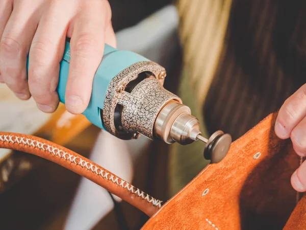 Master bolsa de fabricación de cuero genuino en su taller en casa. El hombre procesa el borde del producto con una máquina amoladora. Un pequeño negocio local. Vista macro . — Foto de Stock