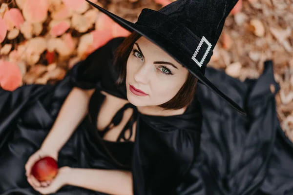 Πορτρέτο της γυναίκας ως μάγισσα στα μαύρα κρατώντας κόκκινο μήλο ως σύμβολο του πειρασμού, δηλητήριο. Παραμύθι έννοια, Απόκριες, cosplay. — Φωτογραφία Αρχείου