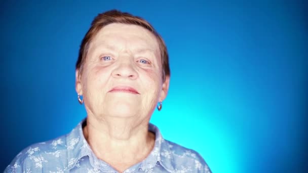 Großmutter lächelt, freut sie sich, an ihrem Geburtstag oder Weihnachten eine Geschenkbox mit Schleife zu bekommen. ältere Rentnerin auf blauem Hintergrund. — Stockvideo