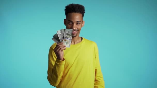 Elégedett afrikai férfi, aki pénzt mutat - amerikai dollár bankjegyek a kék falon. A siker, a nyereség, a győzelem szimbóluma. Lassú mozgás. — Stock videók