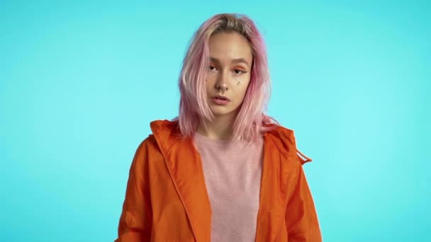 Millennial αινιγματικό όμορφο κορίτσι με ασυνήθιστο ροζ βαμμένο χτένισμα. Χρυσές πούλιες σαν δάκρυα, τρύπημα μύτης. Μυστηριώδης hipster έφηβος σε μπλε φόντο. — Αρχείο Βίντεο