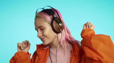 Mavi arka planda turuncu yağmurluklu kulaklıklarıyla sıradışı görünümlü hippi bir kadın. Pembe saçlı güzel kız müzik dinlemekten hoşlanıyor.. 
