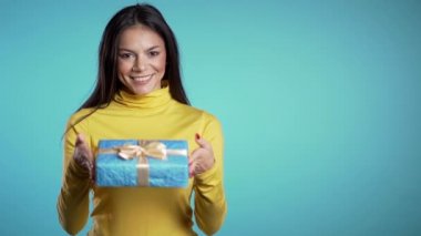 Güzel esmer kadın hediyesini kameraya veriyor. O mutlu, gülümsüyor. Mavi arka plandaki kız. Olumlu tatil görüntüleri