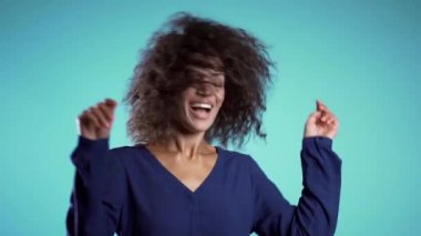 Afro saçlı, güzel Afro-Amerikalı kadın. Stüdyoda mavi arka planda dans edip gülümsüyor. yavaş çekim