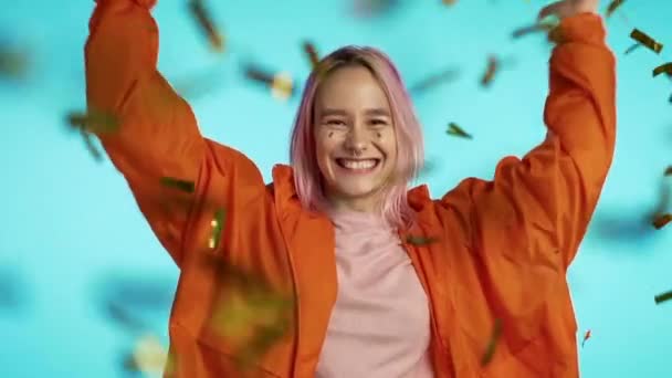 Πολύχρωμο ντυμένο ενθουσιασμένο κορίτσι με ροζ μαλλιά άλμα, διασκεδάζοντας, χαίρεται πάνω από κομφετί βροχή στο στούντιο. Έννοια της ευτυχίας, κόμμα, νίκη. — Αρχείο Βίντεο