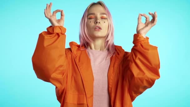 Hipster chica de pelo teñido meditando sobre fondo de pared azul. Mujer tranquila concentrada en la práctica del yoga. Estilo de vida saludable . — Vídeo de stock