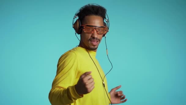 Afro-Amerikaanse man met koptelefoon dansend met handen geïsoleerd op blauwe achtergrond. Feest, muziek, lifestyle, radio en disco concept. — Stockvideo