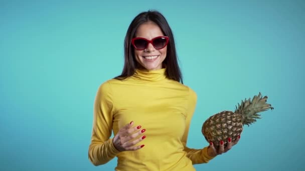 Verspielte junge hispanische Frau wirft Hand in Hand mit frischer Ananas. gesunder exotischer Lebensstil und Ernährungskonzept. Zeitlupe blaues Studiomaterial. — Stockvideo