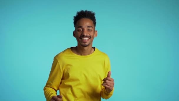 Jonge Afrikaans-Amerikaanse man glimlachend en dansend in goed humeur op blauwe achtergrond.Niet te stoppen plezier, geluk, komisch portret van man geïsoleerd. — Stockvideo