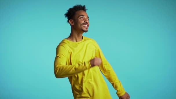 Young african american man smiling and dancing challenge dance in good mood on blue background.Unstoppable fun, happiness, comical portrait of guy isolated. — Stock Video