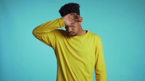 Розчарований афроамериканець у жовтому одязі носить на синьому фоні стіни. Гі втомився від роботи або навчання, розчарований, безпорадний — стокове відео