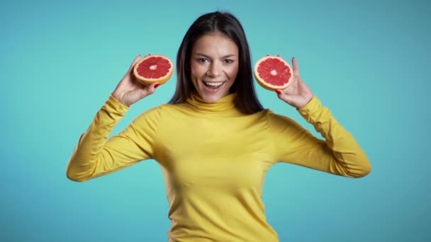Portret van jonge mooie vrouw met twee halve sappige grapefruit op blauwe studioachtergrond. Gezond eten, dieet, antioxidanten concept. — Stockvideo