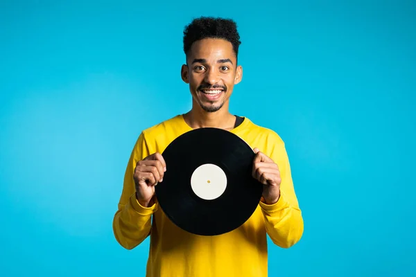 Joven hombre afroamericano guapo en ropa amarilla sosteniendo discos de vinilo en fondo azul. Concepto de música de estilo retro . — Foto de Stock