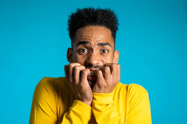 Asustado hombre afroamericano con el pelo rizado miedo de algo y mira a la cámara con grandes ojos llenos de horror sobre fondo azul de la pared . — Foto de Stock