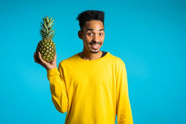 Jovem afro-americano segurando na mão abacaxi fresco. Estilo de vida saudável e exótico e conceito de alimentação. Azul estúdio fundo . — Fotografia de Stock