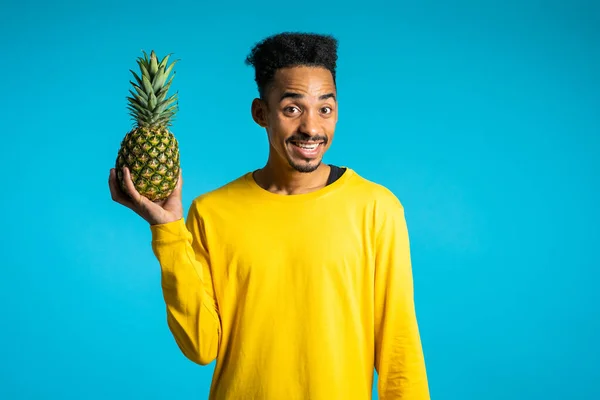 Joven afroamericano sosteniendo en la mano piña fresca. Estilo de vida exótico saludable y concepto de alimentación. Fondo estudio azul . — Foto de Stock