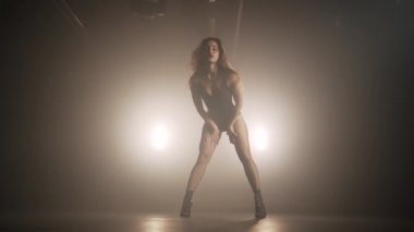 Uzun saçlı, seksi elbiseli güzel bir kadın karanlık odada dans ediyor. Modern dans, yaşam tarzı, yetenekli kız. Yavaş çekim