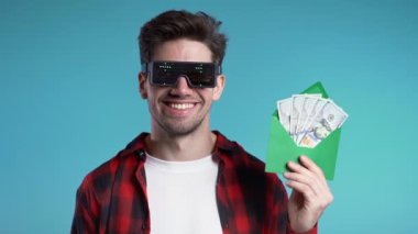 Dolar işaretleri ile parlayan mutlu Avrupalı adam. Zarfta para yazıyor. Mavi duvarda Amerikan doları banknotları. Başarının, kazancının, zaferin sembolü. Yavaş çekim