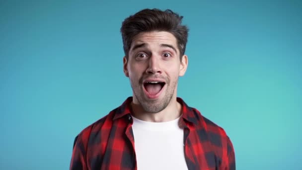 Amazed european man shocked, saying WOW. Handsome guy with stylish hairdo surprised to camera over blue background. — Stock Video