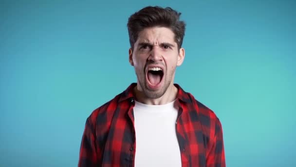 Young european stressed man in red shirt shouting isolated over blue background. Slow motion. Stressed and depressed guy loudly screaming to camera. — Stock Video