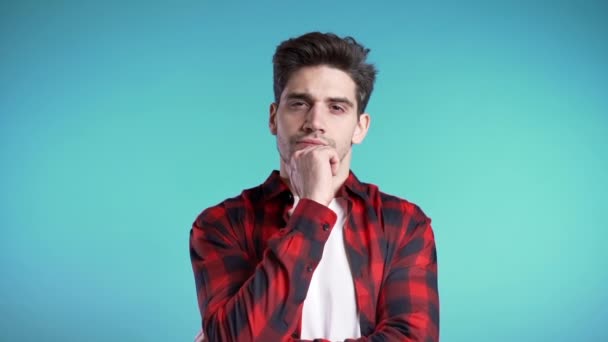 Kopieer ruimte.Denkende man op en rond kijkend op een blauwe achtergrond. Bezorgde contemplatieve gezichtsuitdrukkingen. Mooi mannelijk model in rood shirt. — Stockvideo