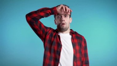 Kırmızılı hayal kırıklığına uğramış Avrupalı adam mavi duvar arka planında yıpranmış. Adam yorgun, çalışmaktan sıkılmış, hayal kırıklığına uğramış, çaresiz.