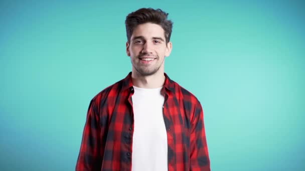 Positive young man smiles to camera. Hipster guy showing thumb up sign over blue background. Winner. Success. Body language. — Stock Video