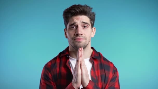 Handsome man in red shirt praying over blue background. European race guy begging someone. Slow motion. — Stock Video