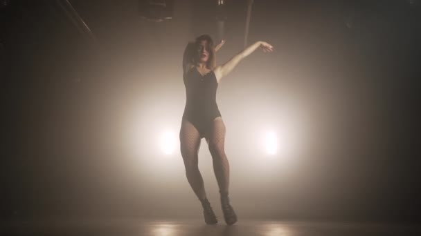 Ung kvinna i svart bodysuit med nät strumpbyxor flyttar plasticly till musik i mörka rummet.Begreppet sexuell dans, koreografi, konst. — Stockvideo