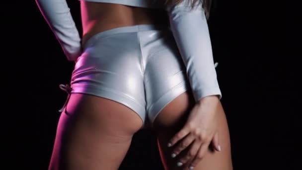 Mulher sexy em shorts de prata curtos dança moderna twerk. Menina tremendo, twerking suas nádegas de perto no fundo preto, luz de néon . — Vídeo de Stock