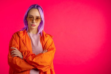Mor saç stili stüdyoda izole edilmiş neşeli, sıradışı bir kızın portresi. Burun piercingli, güneş gözlüklü moda bir kadın. Canlı renkli bir çekim..