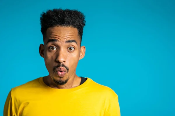 Sorprendido hombre de raza mixta sorprendido, diciendo WOW. Guapo afroamericano chico con afro pelo sorprendido a la cámara sobre fondo azul. Copiar espacio . — Foto de Stock