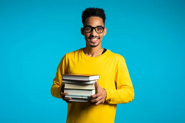 스튜디오의 파란 배경에 있는 아프리카 학생들은 도서관에 있는 책들을 쌓아 둔다. 웃는 남자, 그는 졸업하게 되어 기뻐 합니다.. — 스톡 사진