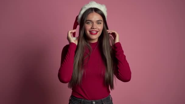 Muchacha atractiva en el sombrero de Santa celebrando la Navidad o Año Nuevo sobre fondo rosa. Mujer bonita feliz sonriendo y divirtiéndose. Movimiento lento . — Vídeo de stock