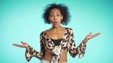 Afro saçlı, leopar desenli güzel bir Amerikalı kadın gülümsüyor, hoş bir şaşkınlık içinde mavi duvar arkasında kameraya dans ediyor.. 