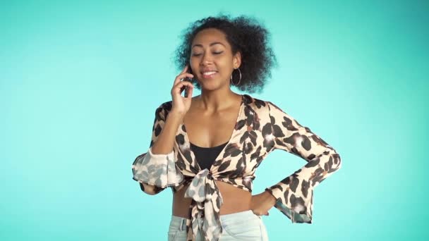 La mujer afroamericana habla por teléfono y sonríe de las bromas de los interlocutores. Maquillaje perfecto, ropa de moda. Movimiento lento . — Vídeo de stock