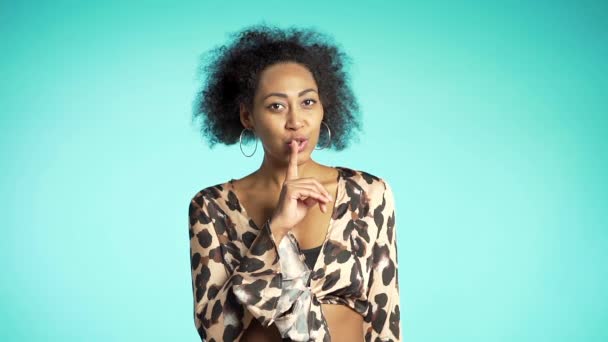 Uma afro-americana a segurar um dedo nos lábios por causa do fundo azul. Gesto de shhh, segredo, silêncio . — Vídeo de Stock
