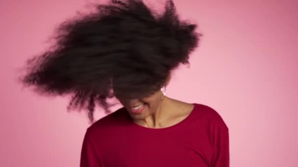 아 프로 헤어를 가진 아름다운 아프리카 계 미국인 여성 이 분홍색 배경에 대항하여 스튜디오에서 웃음 과 춤을 추며 즐거움을 만끽하고 있습니다. 느린 동작 — 비디오