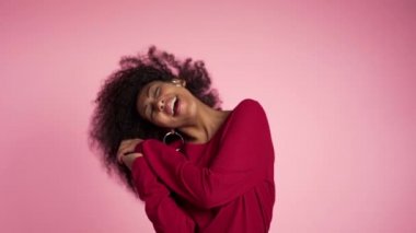 Afro saçlı güzel Afro-Amerikalı kadın stüdyoda pembe arka planda gülüp dans ediyor. yavaş çekim